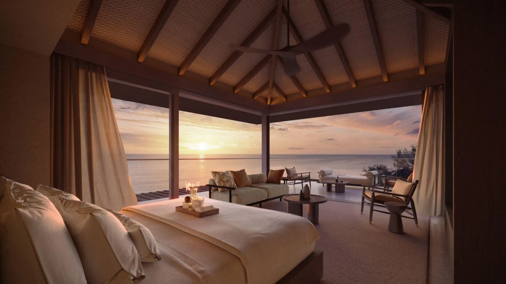 A villa bedroom opening onto the ocean at sunset