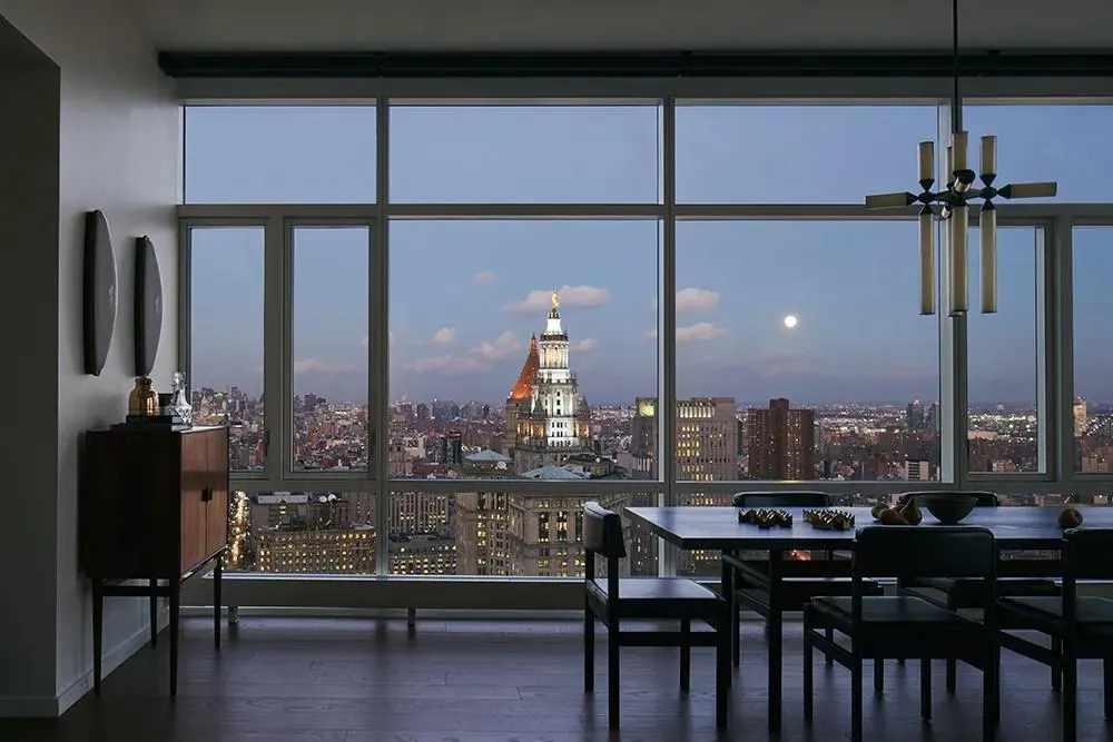 A residence dining table set against floor-to-ceiling windows at dusk