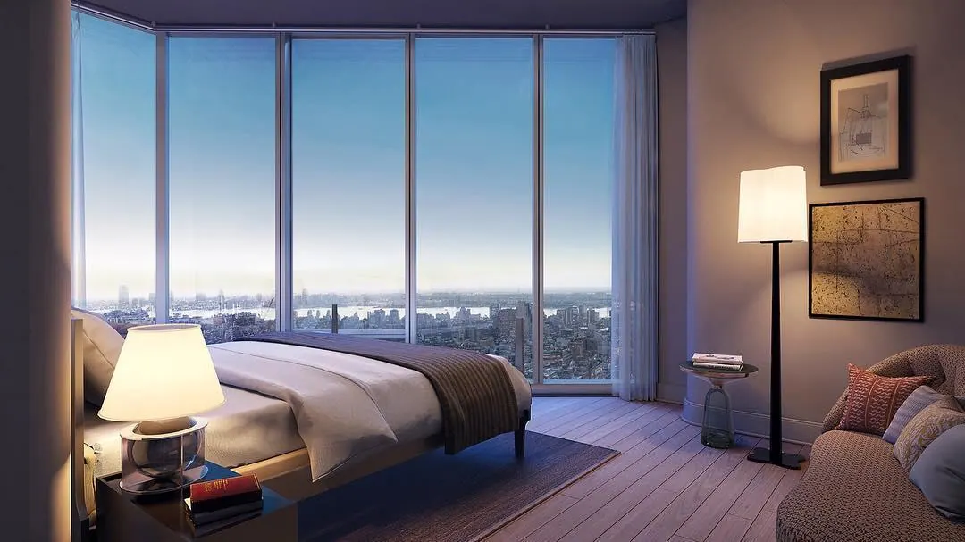 A bedroom with a wall of glass overlooking the river at dusk